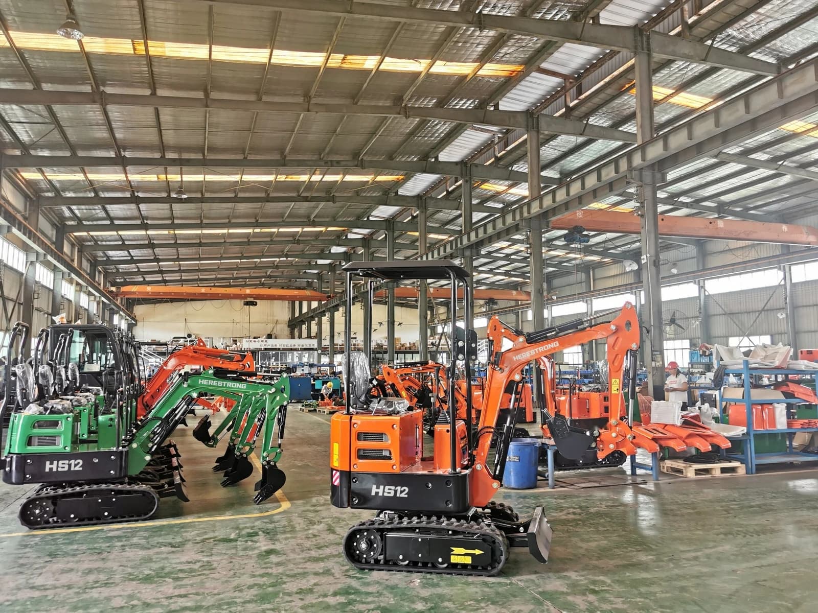 Green and orange HS12 excavators in the HERESTRONG workshop
